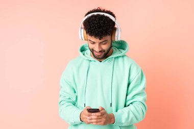 Genç Faslı bir adam pembe arka planda izole edilmiş müzik dinliyor ve cep telefonu arıyor.