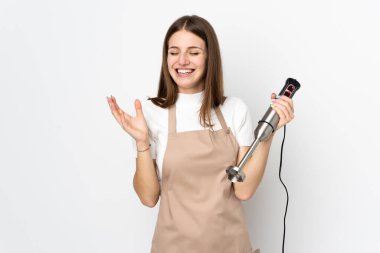 Beyaz arka planda izole edilmiş el blenderi kullanan genç kadın gülüyor.