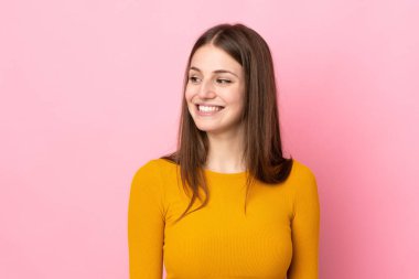 Pembe arka planda soyutlanmış genç beyaz kadın yana bakıyor ve gülümsüyor.