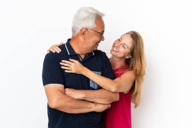 Orta yaşlı çift, beyaz arka planda gülüp sarılıyorlar.