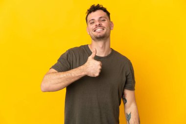 Sarı arka planda izole edilmiş beyaz, yakışıklı genç bir adam baş parmak işareti yapıyor.