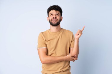 Faslı genç bir adam mavi arka planda izole edilmiş. Harika bir fikre işaret ediyor.