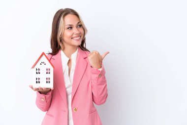 Rus emlakçı elinde beyaz arka planda izole edilmiş bir oyuncak ev tutuyor. Ürünü sunmak için yan tarafa bakıyor.