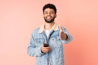 Pembe arka planda izole edilmiş cep telefonu kullanan genç Faslı adam iyi bir anlaşma için el sıkışıyor.