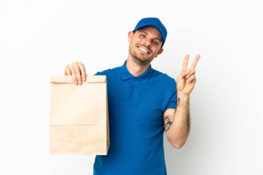 Brezilyalı, beyaz arka planda izole edilmiş bir paket yiyecek alıyor gülümsüyor ve zafer işareti gösteriyor.