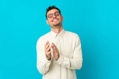 Beyaz tenli yakışıklı adam mavi arka planda izole edilmiş bir konferansta sunumdan sonra alkışlıyor.