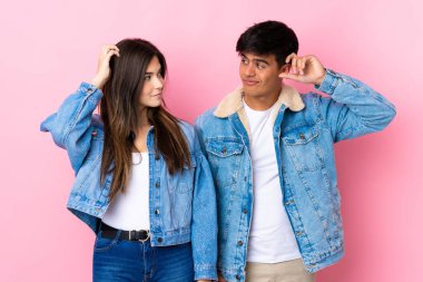 Soyutlanmış pembe arka planı olan genç bir çift kafalarını kaşırken şüphe duyuyorlar.