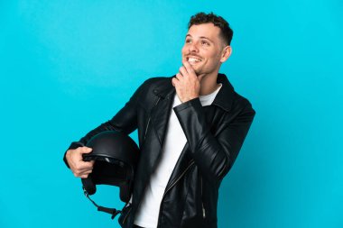 Motosiklet kasklı beyaz adam mavi arka planda izole edilmiş gülümserken yukarı bakıyor.