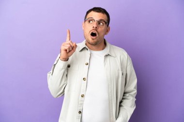 İzole edilmiş mor arka planı olan Brezilyalı bir adam bir fikrin parmağı yukarı kaldırdığını düşünüyor.