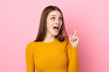 Pembe arka planda izole edilmiş genç beyaz bir kadın, bir fikrin işaret ettiğini düşünüyor.