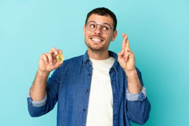 Brezilya 'lı bir adam Bitcoin' i izole edilmiş mavi arka planda tutarken şans diliyor ve en iyisini diliyor