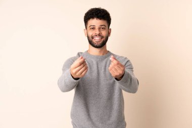 Bej arka planda izole genç Faslı adam para hareketi yapıyor.