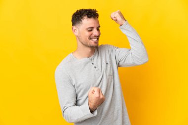 Sarı arka planda izole edilmiş beyaz yakışıklı bir adam zaferi kutluyor.