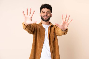 Faslı genç bir adam bej arka planda izole edilmiş. Parmaklarıyla ona kadar sayıyor.
