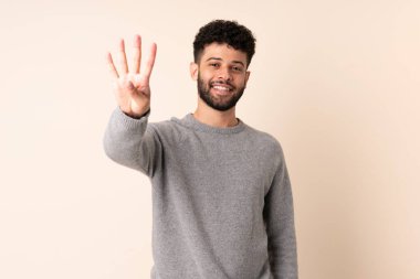 Bej arka planda izole edilmiş genç Faslı adam mutlu ve parmakları olan dört kişi sayıyor.