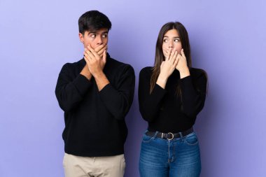 İzole edilmiş mor arka planı olan genç bir çift elleriyle ağzını kapatıyor.