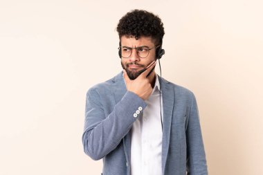 Faslı bir pazarlamacı bej arka planda izole edilmiş bir kulaklıkla çalışıyor. Şüpheleri ve düşünceleri var.