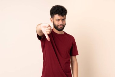 Bej arka planda izole edilmiş genç Faslı adam, olumsuz ifade ile baş parmağını aşağı gösteriyor.