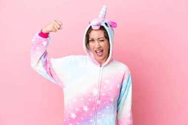 Pembe arka planda izole edilmiş tek boynuzlu at pijamalı beyaz bir kadın güçlü bir jest yapıyor.