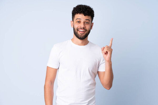 Молодой марокканский человек изолирован на синем фоне, думая, что идея указывает пальцем вверх