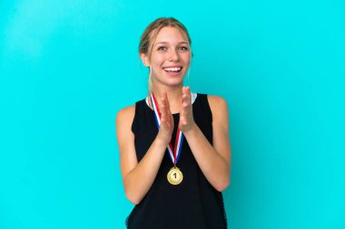 Mavi arka planda madalyaları olan beyaz bir kadın bir konferanstan sonra alkışlıyor.