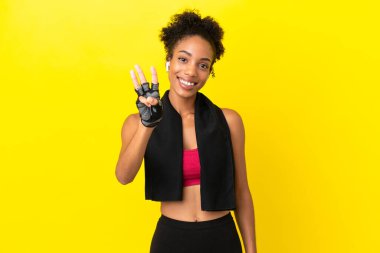 Sarı arka planda yalnız yaşayan genç Afrikalı sporcu kadın mutlu ve parmaklarıyla üçe kadar sayıyor.