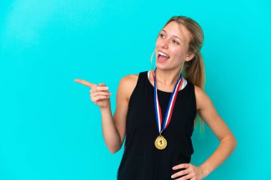 Mavi arka planda madalyaları olan genç beyaz bir kadın parmak göstererek bir ürün sunuyor.