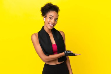 Genç Afrikalı spor kadını sarı arka planda izole edilmiş bir şekilde bir fikir sunarken gülümsüyor