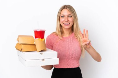 Mavi arka planda şişman yiyecekler tutan beyaz kadın mutlu ve parmaklarıyla üçe kadar sayıyor.