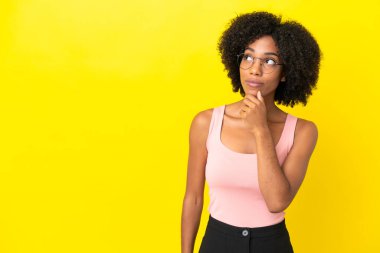 Genç Afrikalı Amerikalı kadın sarı arka planda izole edilmiş ve yukarı bakıyor.