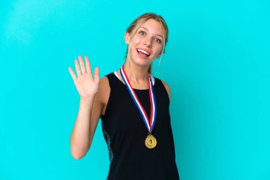 Mavi arka planda madalyalı beyaz bir kadın. Mutlu bir ifadeyle selamlıyor.