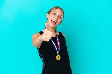 Mavi arka planda madalyalı beyaz bir kadın var. Başparmakları havada. Çünkü iyi bir şey oldu.