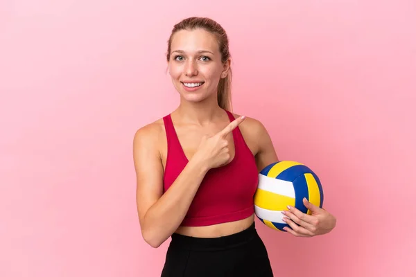 若いです白人女性は 製品を提示する側を指してピンクの背景に孤立バレーボールをプレイ — ストック写真