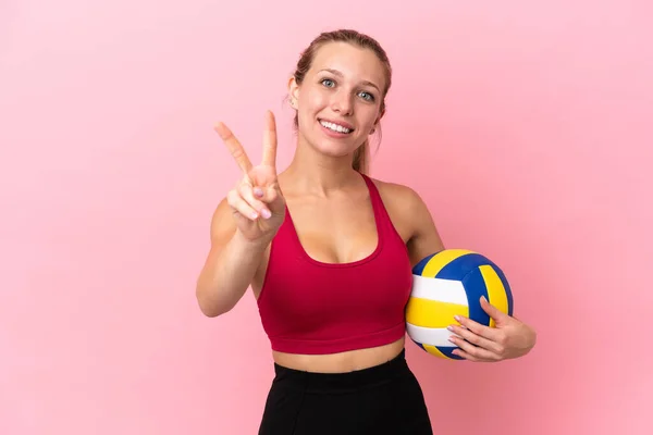 Молодая Кавказка Играет Волейбол Розовом Фоне Улыбаясь Показывая Знак Победы — стоковое фото