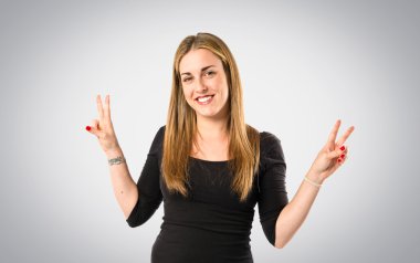 Sarışın kız gri arka planda zafer jesti yapıyor.