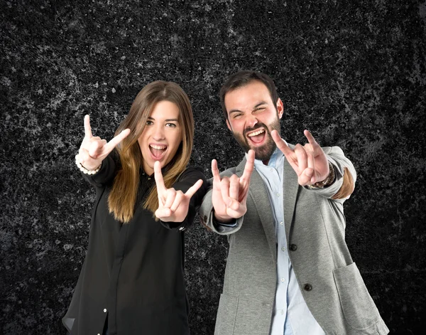 Casal fazendo o sinal de chifre sobre fundo preto — Fotografia de Stock