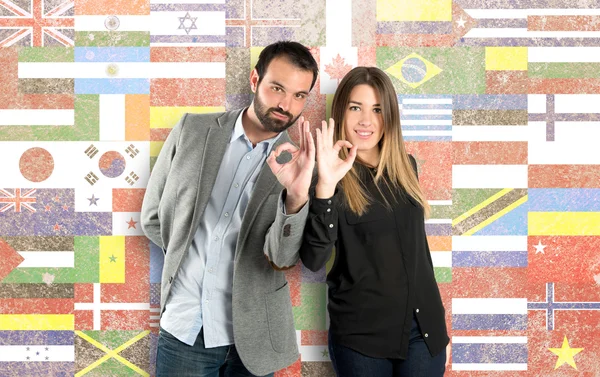 Couple making Ok sign over flags background — Stock Photo, Image