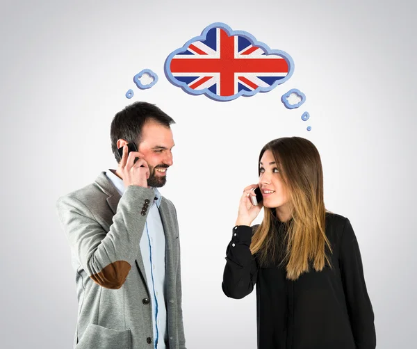 Couple talking to mobile over grey background. — Stock Photo, Image