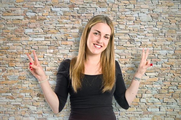 Blonde girl doing victory gesture over textured background — Stock Photo, Image