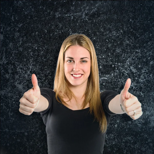 Blond meisje maken ok teken op zwarte achtergrond — Stockfoto