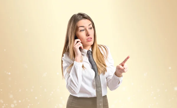 黄土色の背景の上の携帯電話で話している若い女の子 — ストック写真