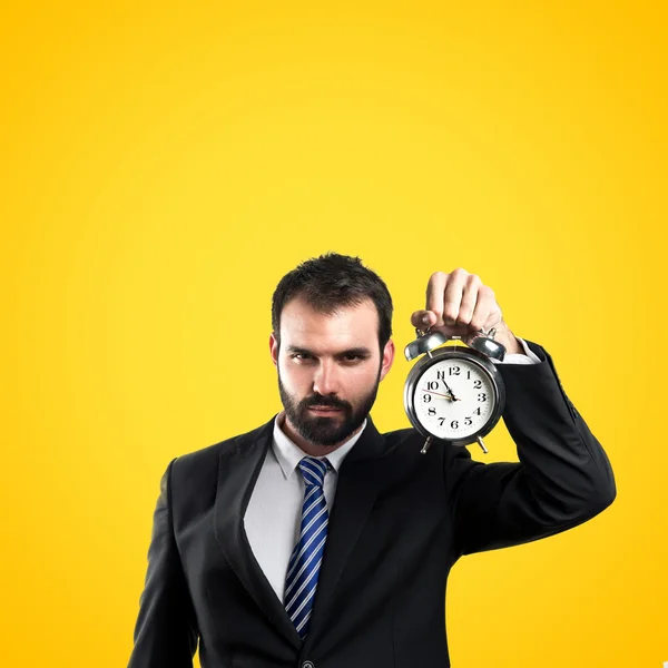 Young businessman holding an antique clock over yellow background — Stock Photo, Image