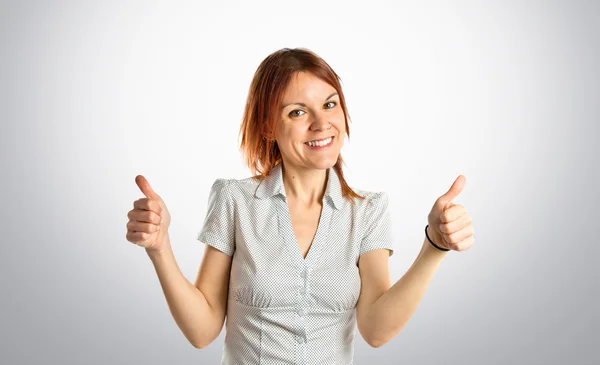 Hübsches junges Mädchen mit hochgereckten Daumen über grauem Hintergrund — Stockfoto