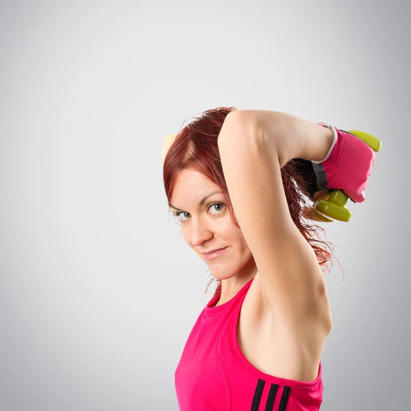 Redhead girl doing weightlifting over grey background, — Stock Photo, Image