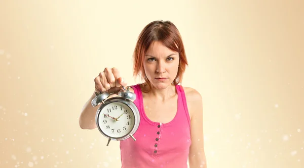 Chica pelirroja seria sosteniendo un reloj sobre fondo ocre —  Fotos de Stock