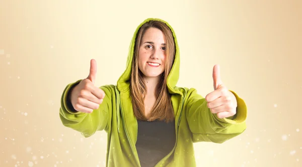 Menina bonita com polegares para cima sobre fundo ocre — Fotografia de Stock