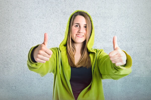 Menina bonita com polegares para cima sobre fundo texturizado — Fotografia de Stock