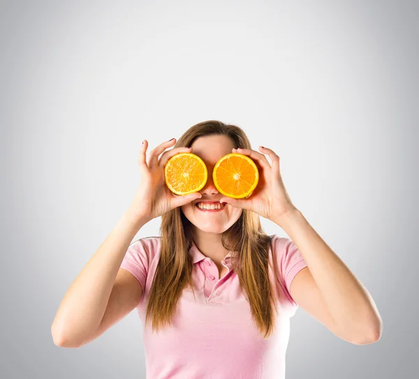 Girl with oranges in her eyes over grey background — Stock Photo, Image