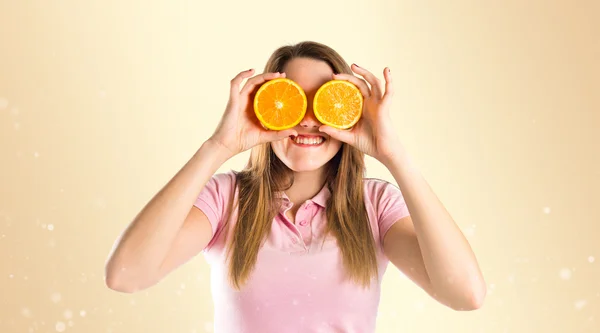 Girl with oranges in her eyes over ocher background — Stock Photo, Image