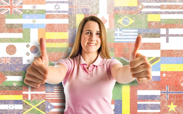 Young girl making Ok sign over flags background — Stock Photo, Image